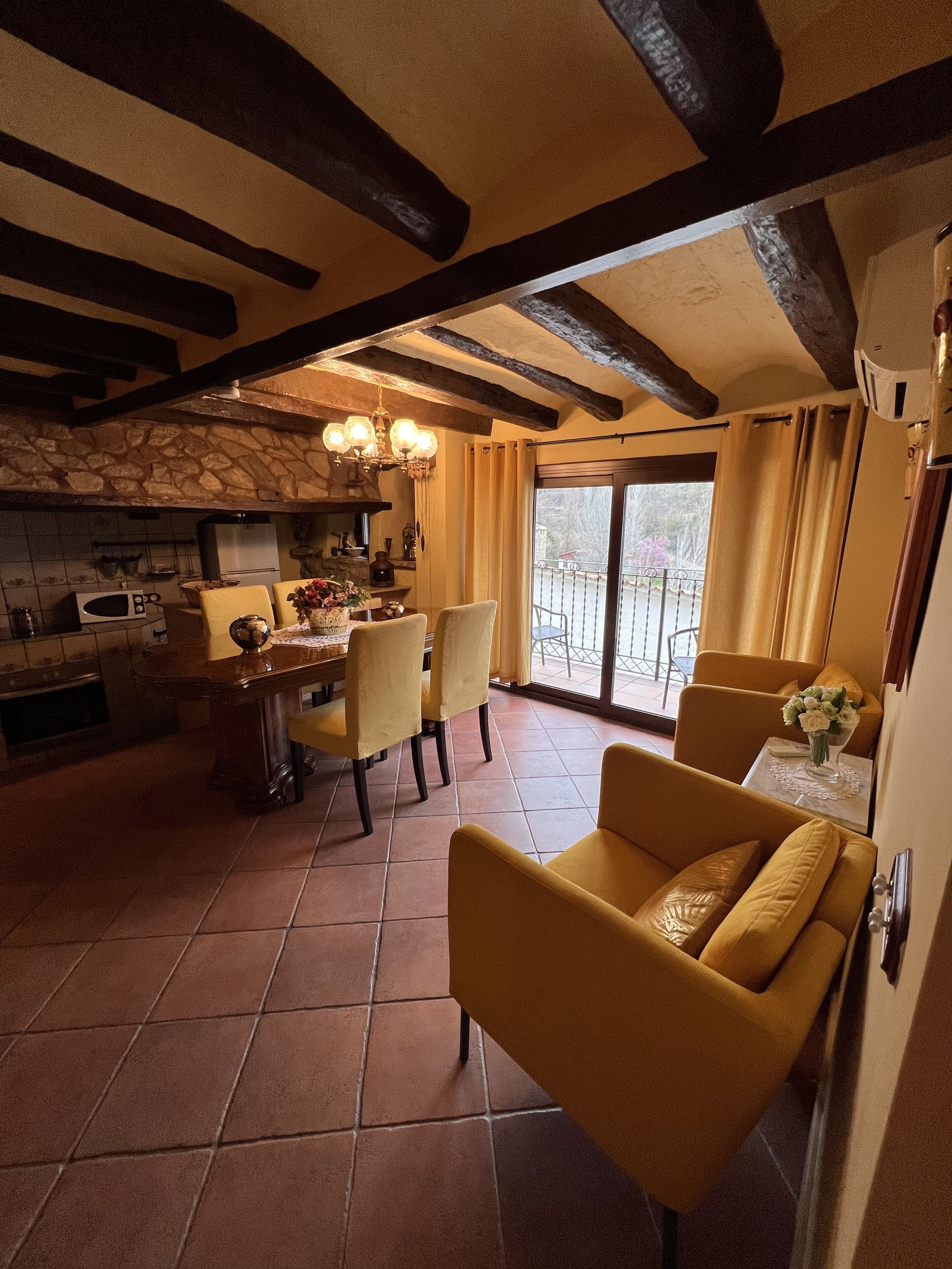 Una cocina amplia con pared de piedra, un comedor con sillas amarillas y un balcón con vistas.
