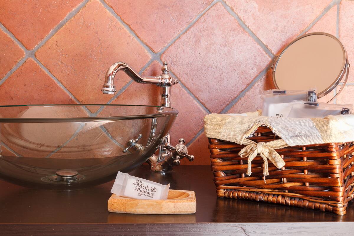 A bathroom with a large glass bowl sink, a wooden basket, and a mirror.