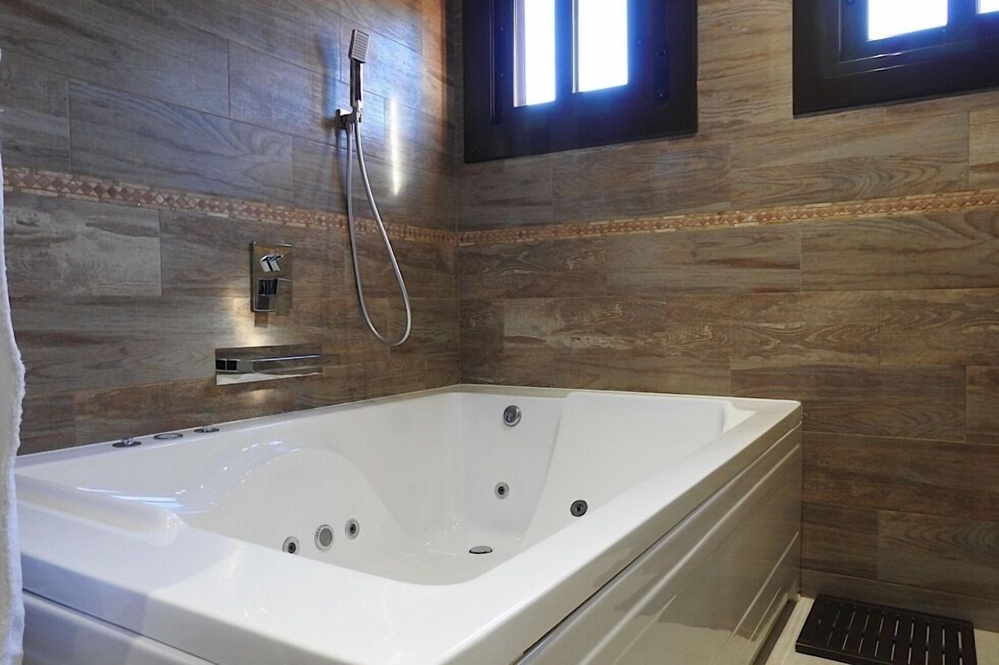 Ein modernes Badezimmer mit einer großen Badewanne, einer Duschbrause und einem Fenster.
