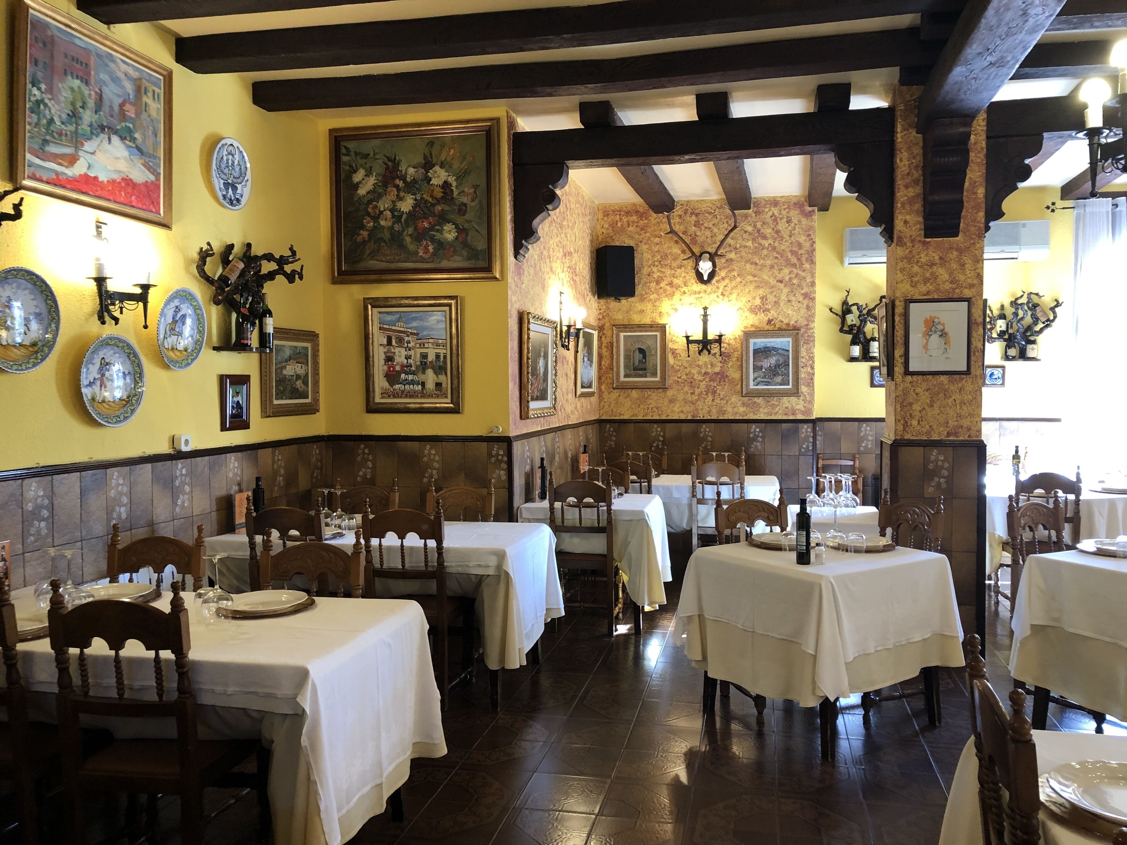 Interior de un restaurante con varias mesas y sillas, obras de arte enmarcadas en las paredes y piso de baldosas.