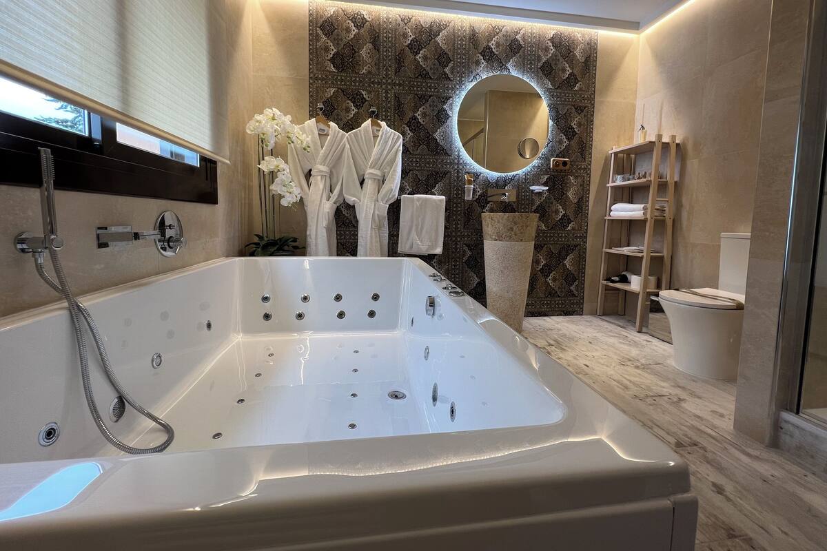 A modern bathroom with a large bathtub, a round mirror, and a decorative wall.