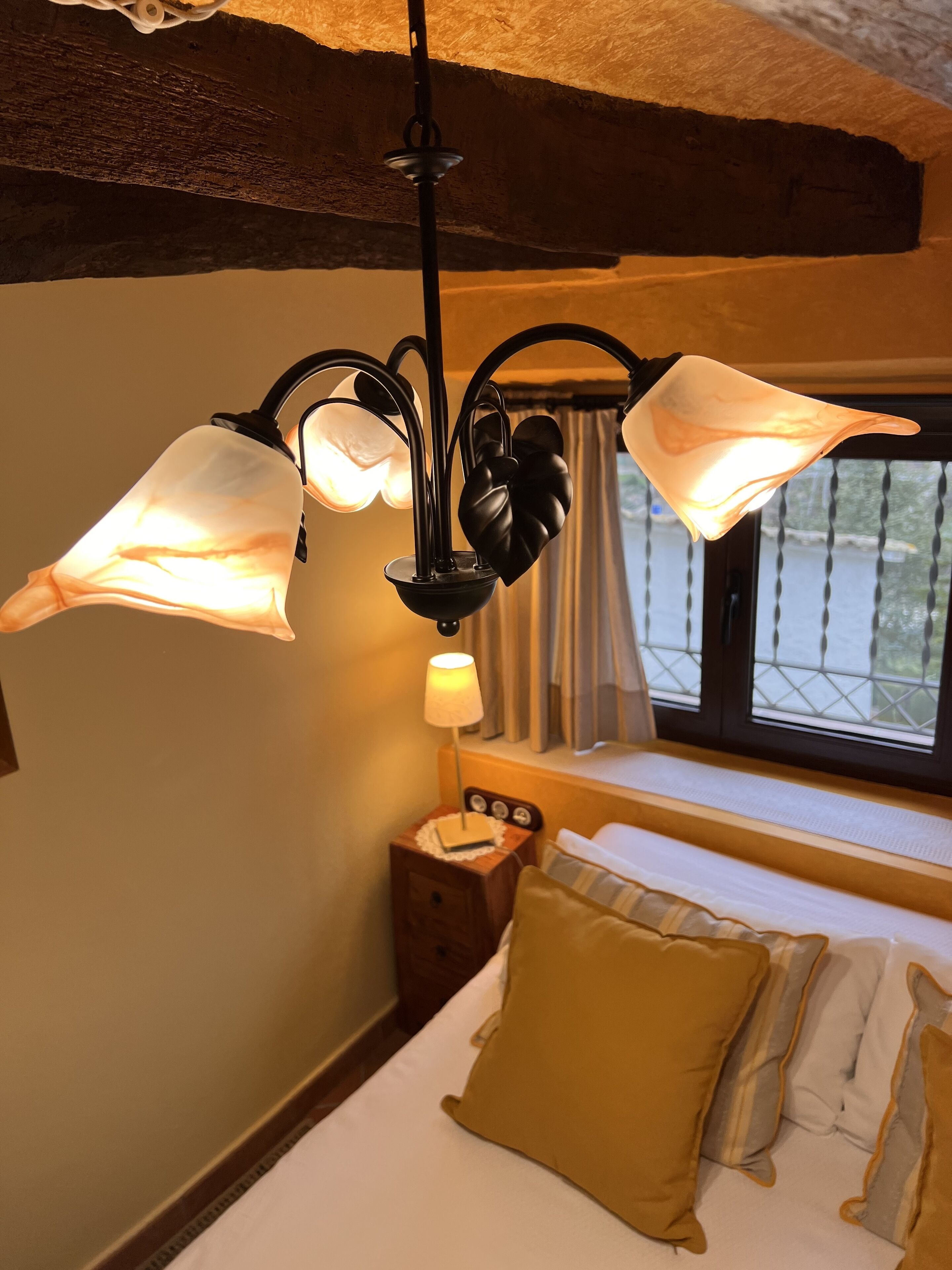 A bedroom with a bed, a bedside table, a lamp, and a window with curtains.
