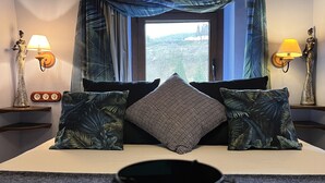Une chambre avec un grand lit, deux tables de chevet avec des lampes, une fenêtre avec des rideaux et une vue sur l’extérieur.