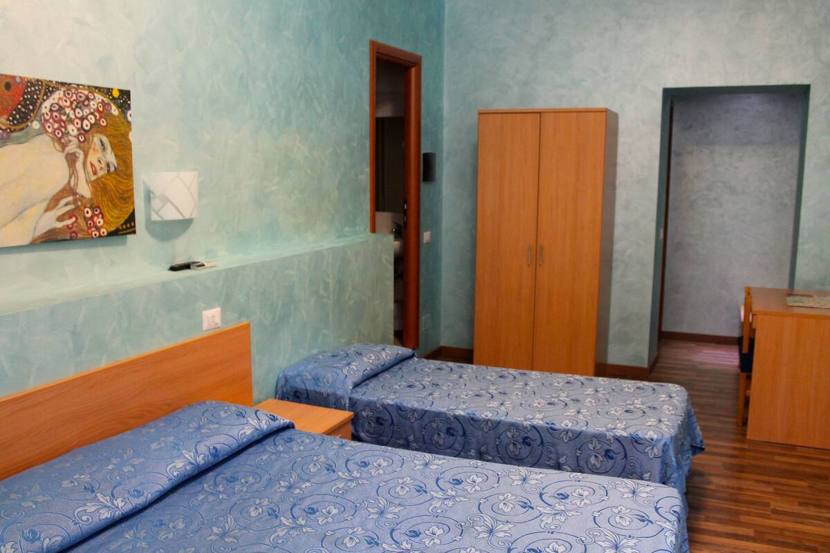 Une chambre avec deux lits, une armoire en bois, un tableau au mur et une petite table.
