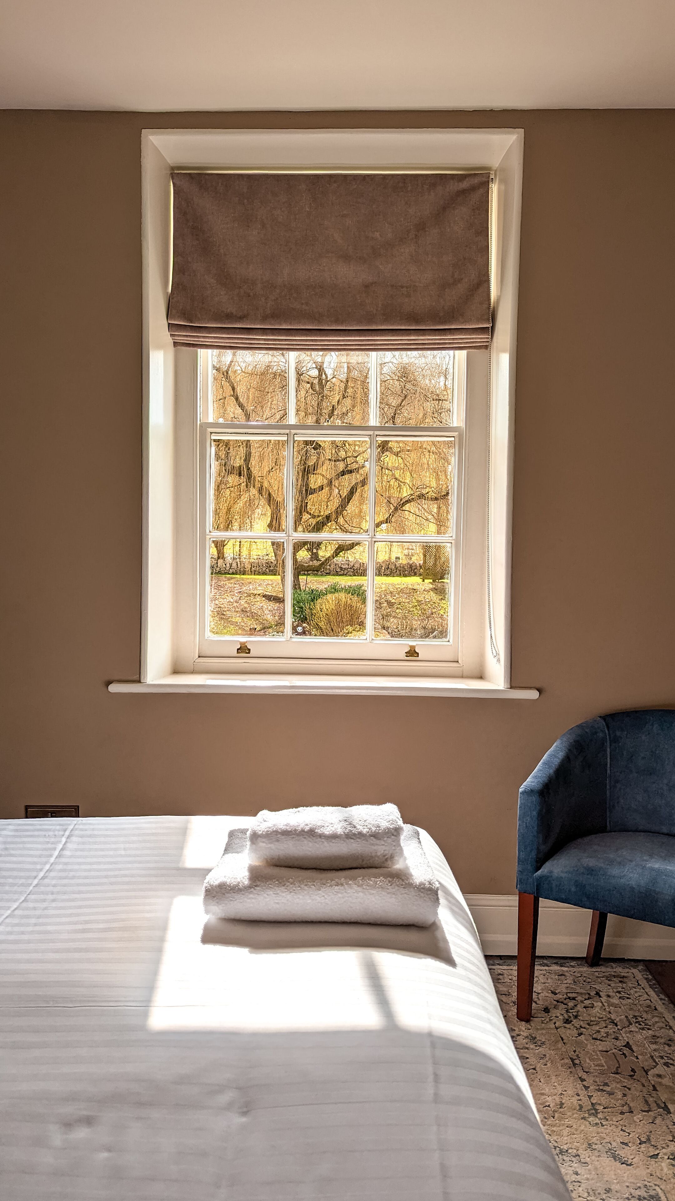 A bedroom with a large window, a bed with white linens, and a blue chair.