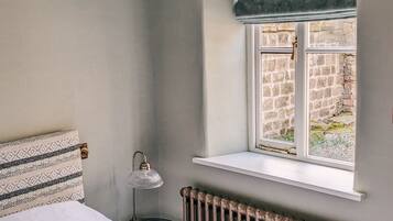 A bedroom with a bed, a radiator, a window with a view of a brick wall, and a patterned pillow.