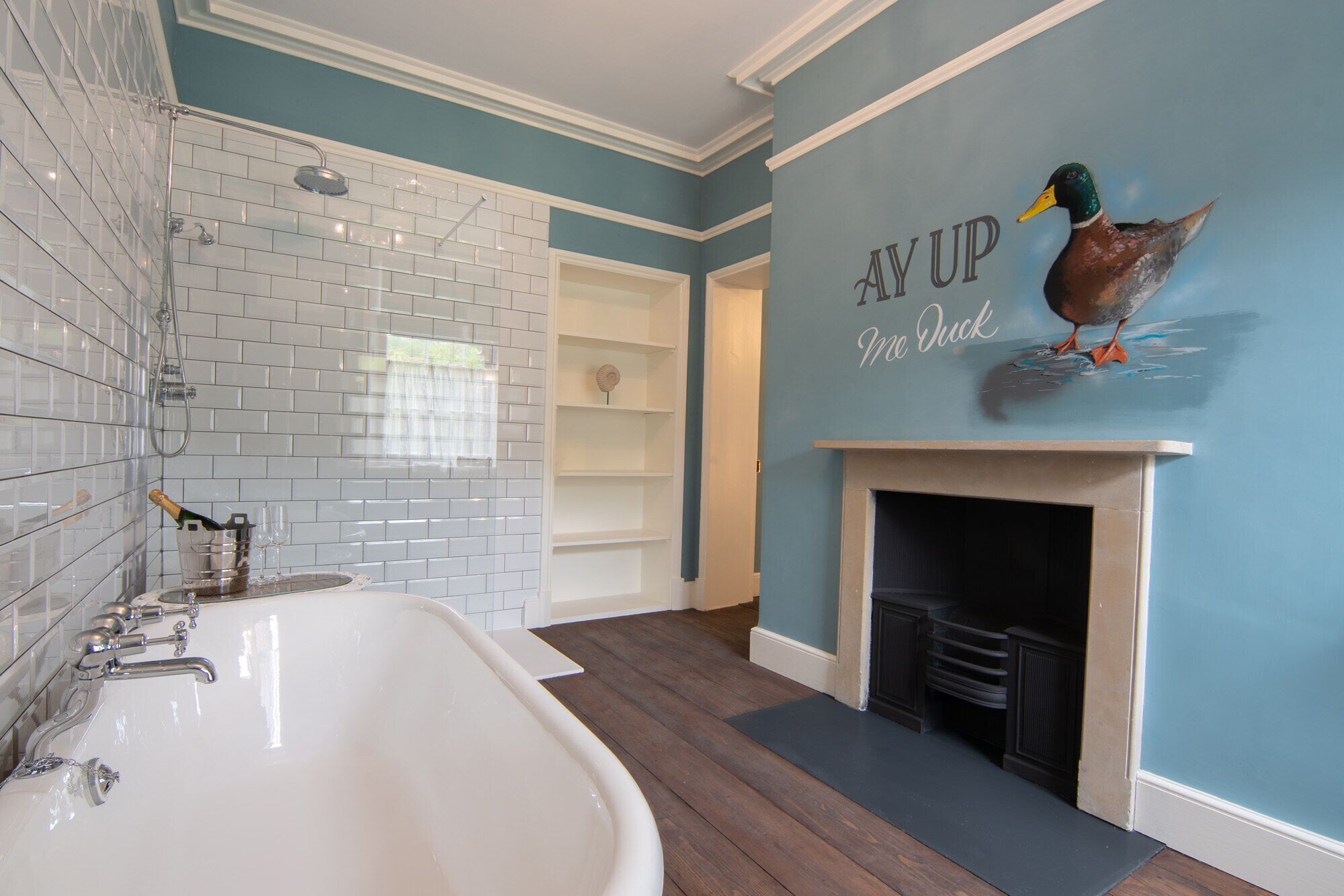 A bathroom with a white bathtub, a shower, and a wall with a duck mural.