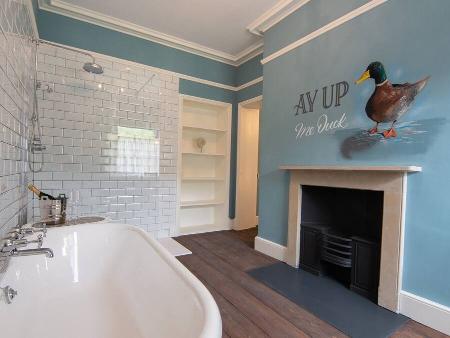 Un baño con una bañera blanca, ducha y un mural de patos en la pared.