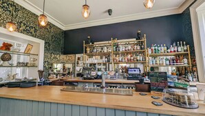 A bar with a wooden counter, shelves of liquor bottles, and a cash register. - Oakhill  (Matlock)