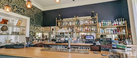 Un bar con mostrador de madera, estantes llenos de botellas de licor y una caja registradora.