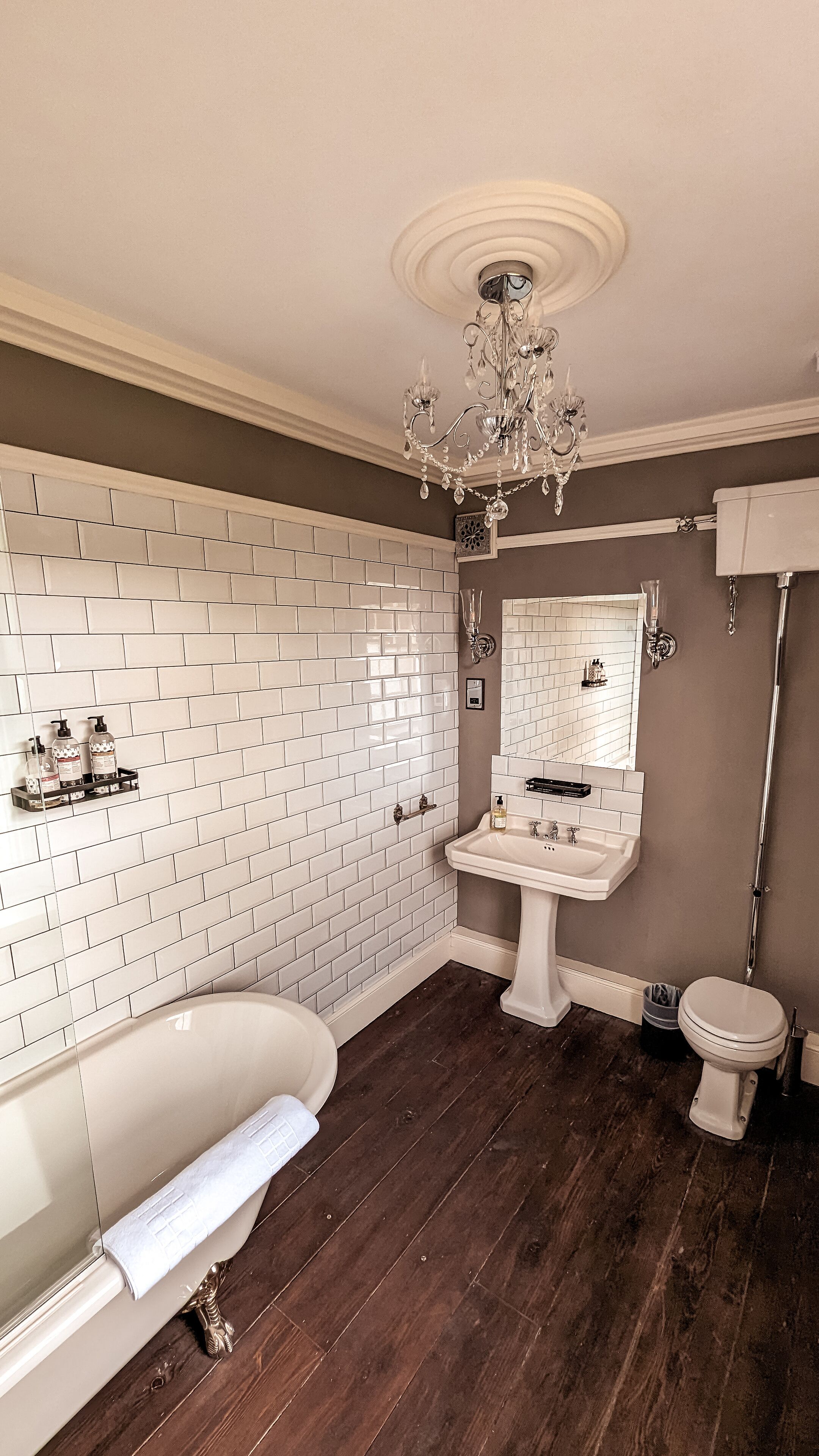 Un baño con una bañera blanca, un lavabo pedestal, un inodoro y una araña.