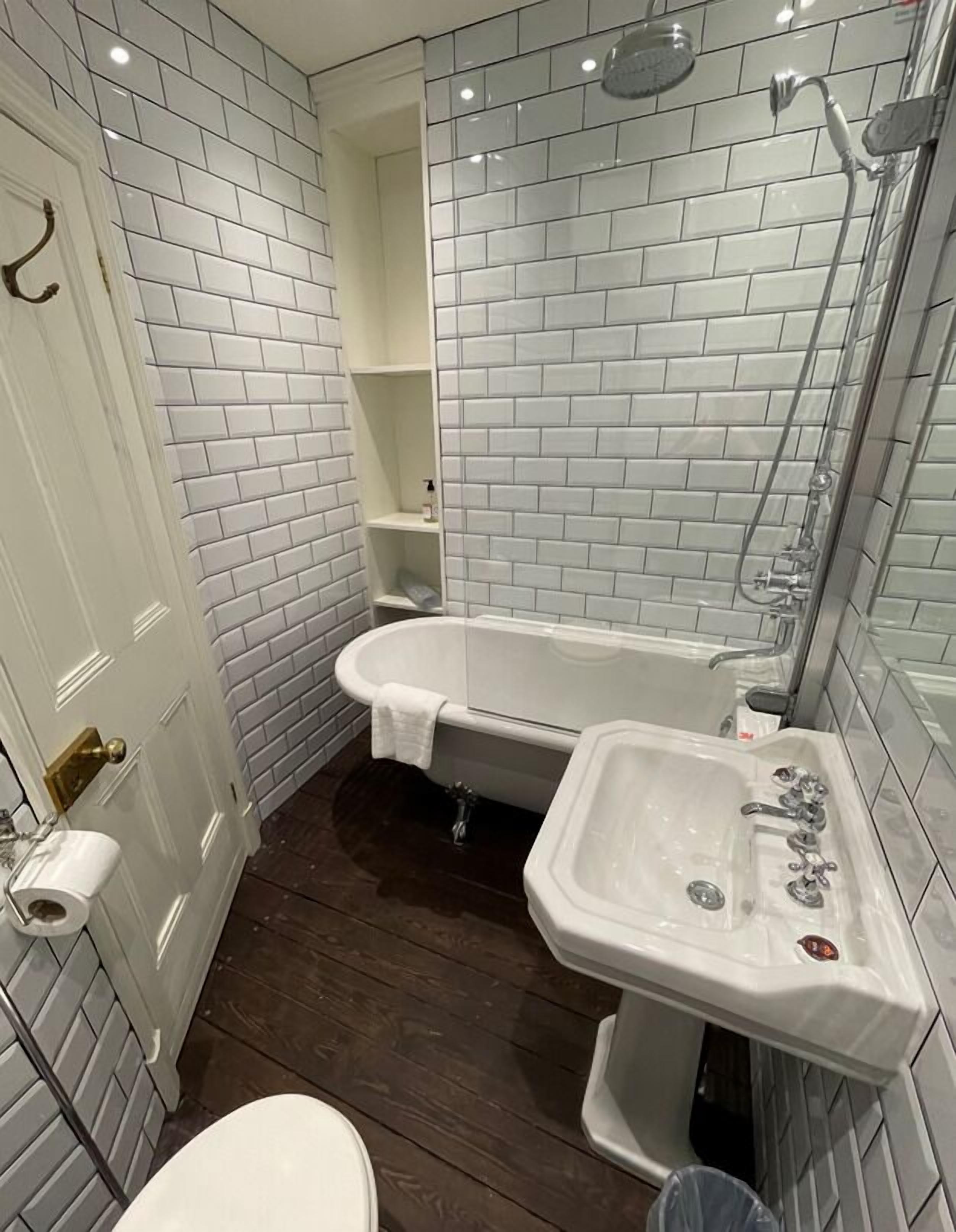 A bathroom with white subway tiles, a bathtub, a sink, and a toilet.