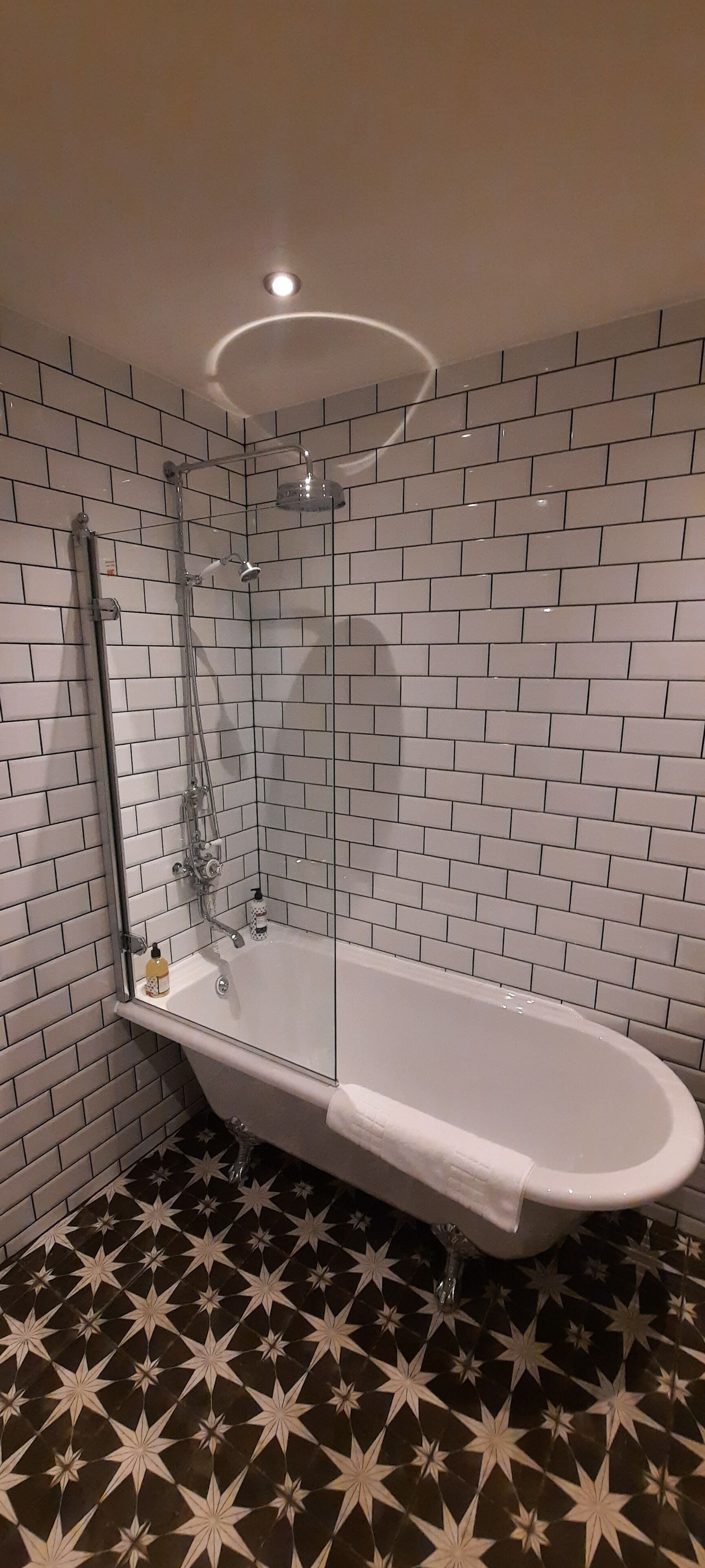 Un baño con una bañera independiente, ducha con mampara de vidrio y suelo de baldosas con diseño de estrellas.