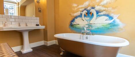 Une salle de bain avec une baignoire sur pieds, un lavabo blanc posé sur un piédestal et une fresque murale représentant des cygnes.