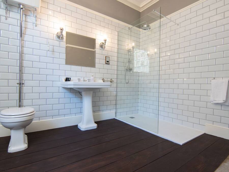 Un baño con azulejos blancos tipo metro, un lavamanos pedestal, un inodoro y una mampara de cristal para la ducha.