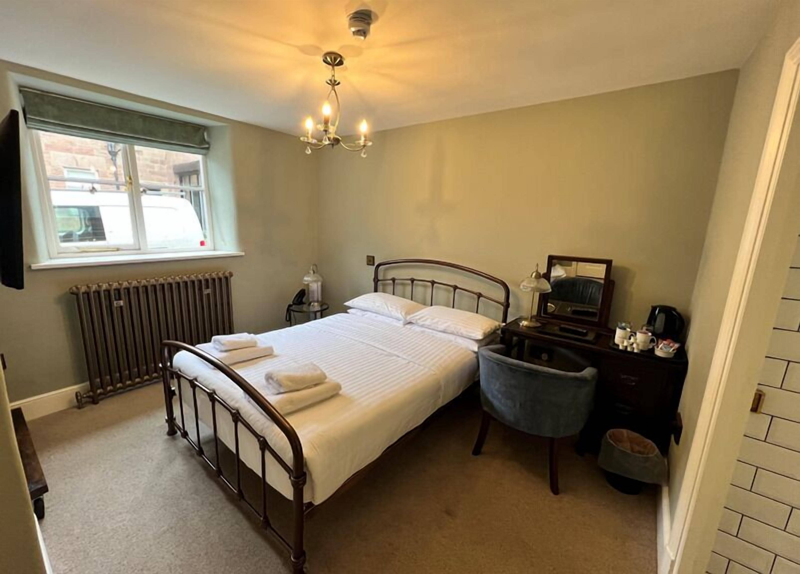 A neatly arranged bedroom with a bed, bedside table, chair, and a radiator.