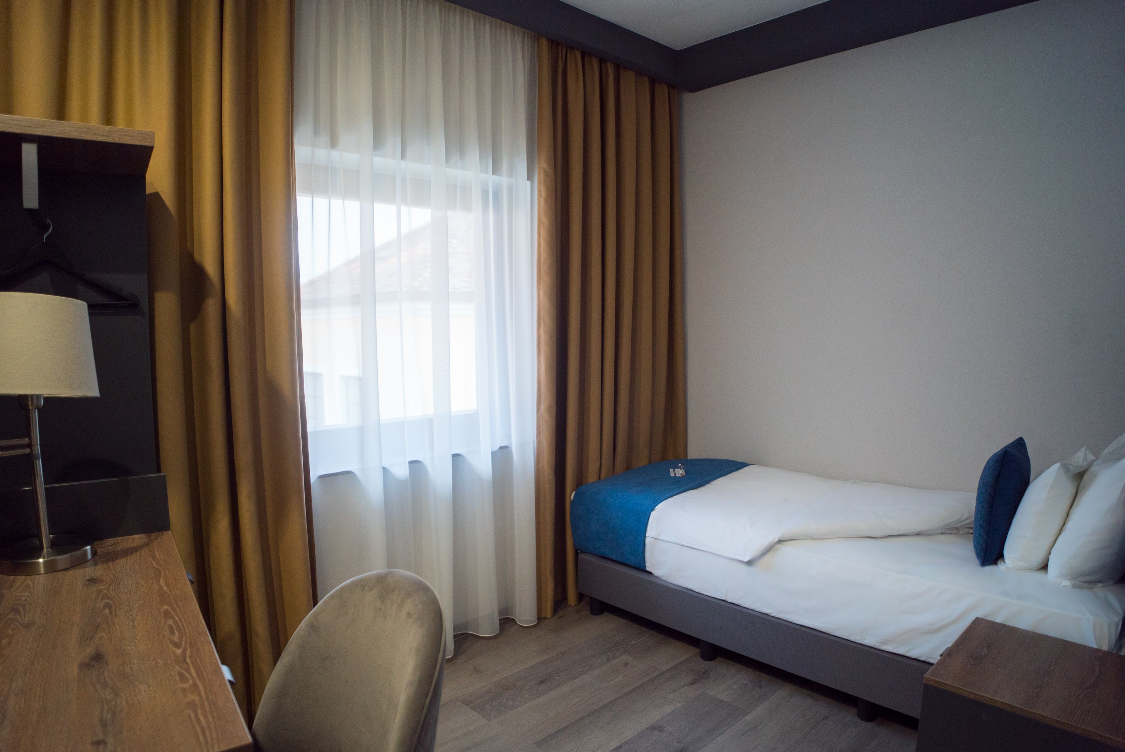 Ein Hotelzimmer mit einem Bett, einem Schreibtisch, einem Stuhl und einem Fenster mit Vorhängen.