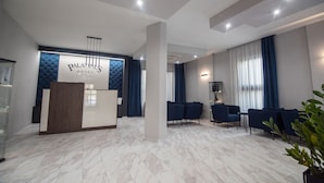 A hotel reception area with a modern design, featuring a reception desk, seating area, and a large window with curtains.