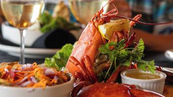 A lobster dish with a lemon wedge, salad, and a small bowl of sauce on a wooden board.