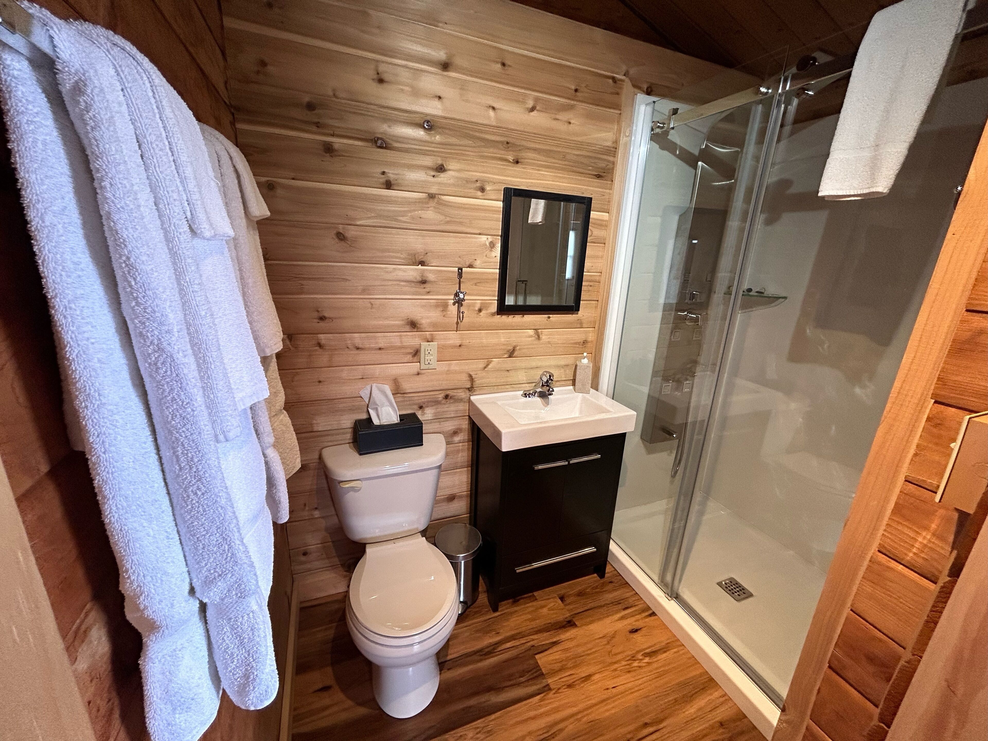A wooden-paneled bathroom with a toilet, sink, and glass shower enclosure.