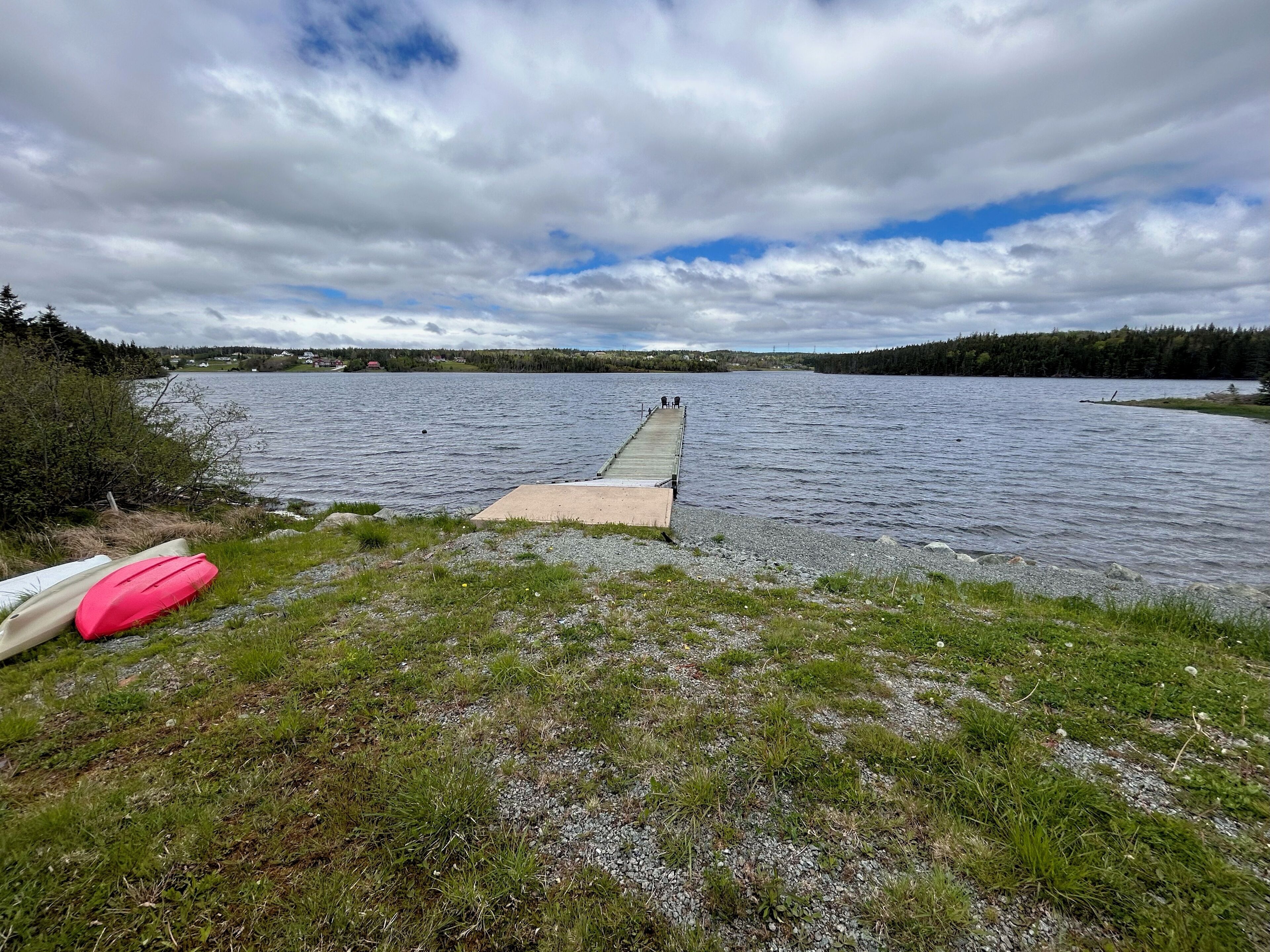 Un muelle que se adentra en un lago con orilla cubierta de césped y kayaks.