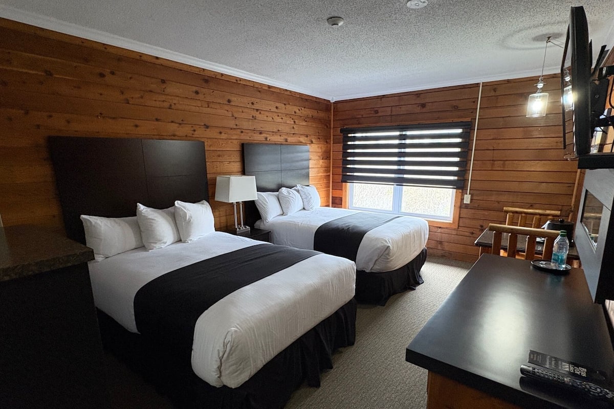 Habitación de hotel con dos camas, un escritorio y una ventana con persianas.