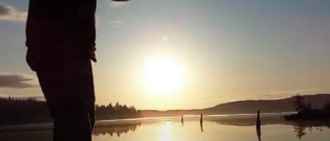 Una persona de pie junto a un cuerpo de agua tranquilo al atardecer.