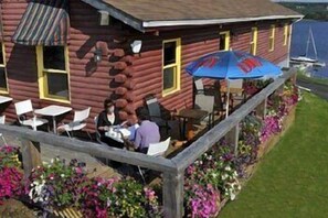 A log cabin with outdoor seating and a flower garden. - Bras d'Or Lakes Inn (St. Peters)
