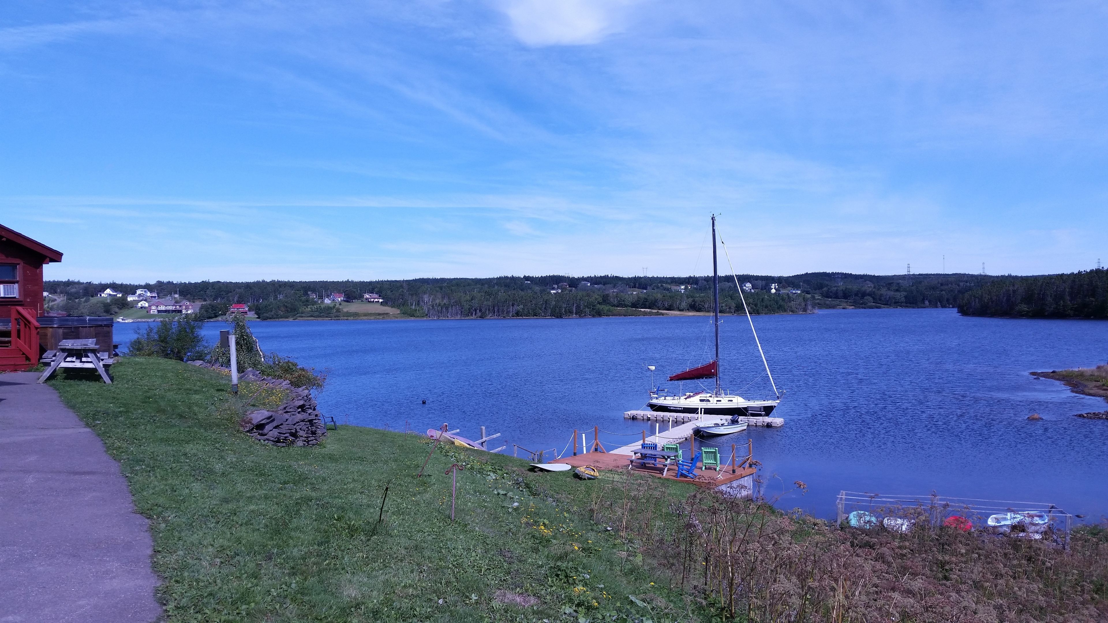 A lakeside view with a dock, a sailboat, and a red building.
