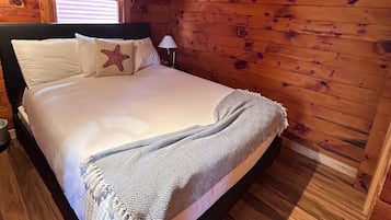 A wooden cabin bedroom with a bed, a starfish pillow, a lamp, and a window with blinds.