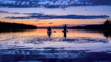 A serene lake at sunset with two kayaks and a person standing on the shore.