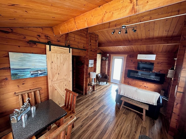 Interior de una cabaña de madera con comedor, chimenea, televisor y un cuadro en la pared.