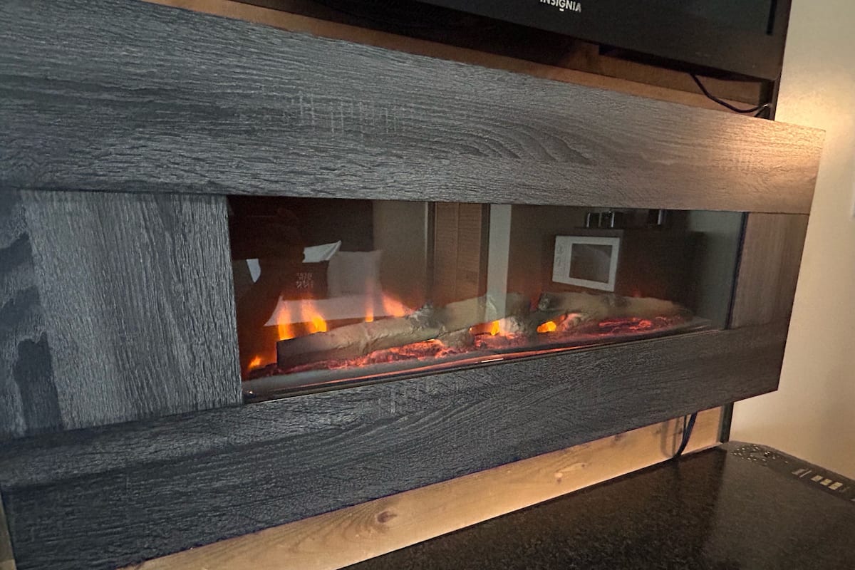 Una chimenea con un marco de madera oscura y un frente de vidrio, mostrando fuego en su interior.