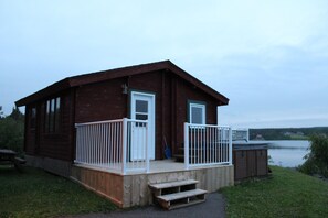 A wooden cabin with a deck, a door, and a window. - Bras d'Or Lakes Inn (St. Peters)