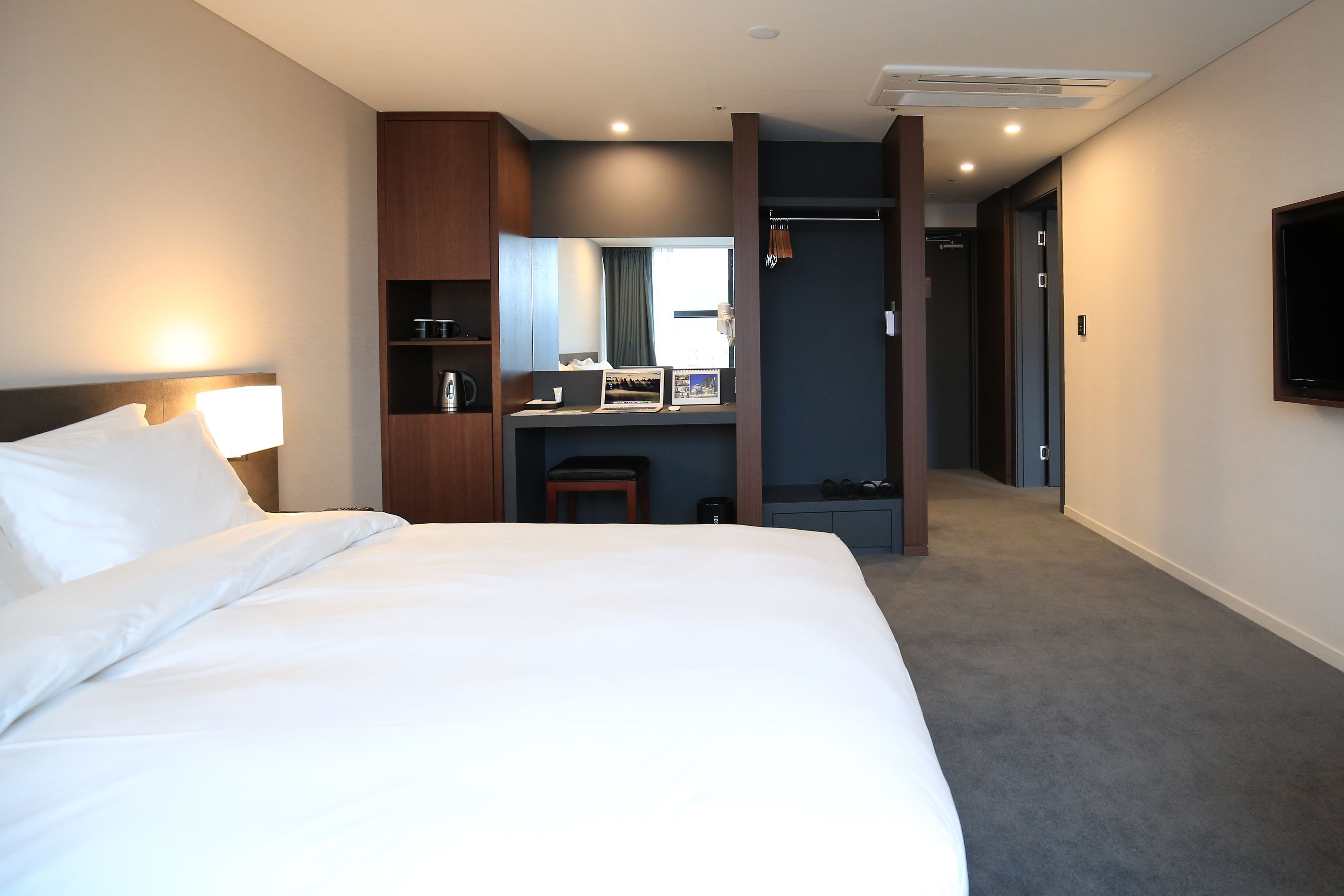A hotel room with a large bed, a desk with a chair, a mirror, a television, and a wardrobe.