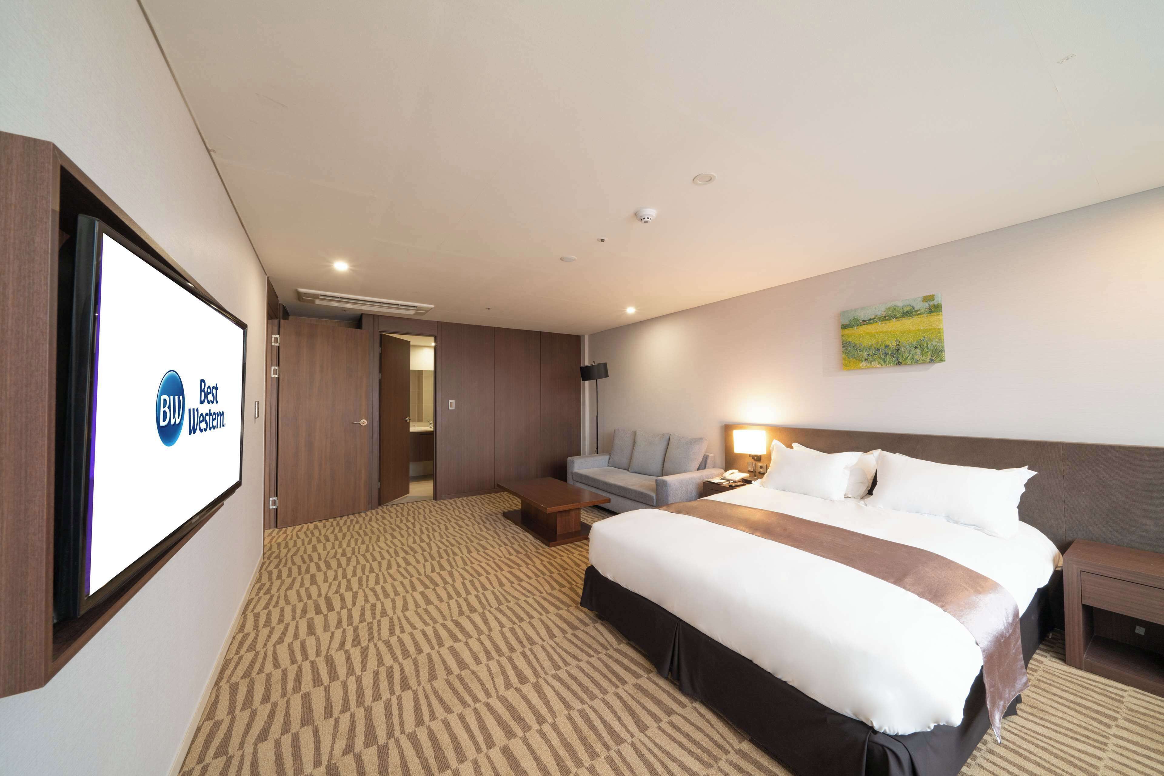 Une chambre d’hôtel équipée d’un grand lit, d’un canapé, d’un bureau et d’un écran de télévision affichant le logo de Best Western.
