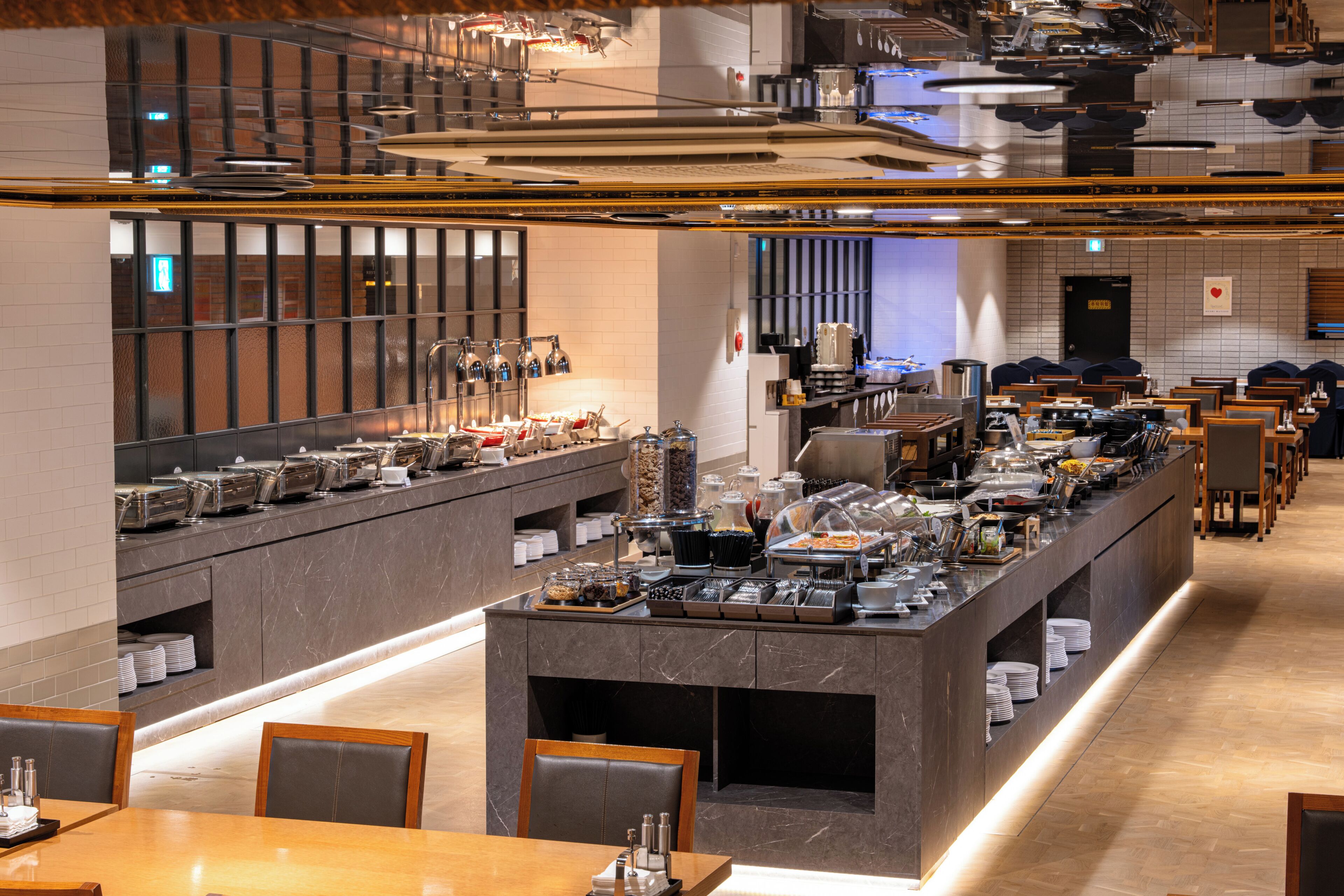 Un área para el desayuno tipo bufé con varias estaciones de servicio, diferentes disposiciones de asientos y un diseño de interiores moderno.