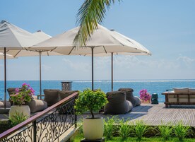 Um terraço à beira-mar com área de estar ao ar livre, guarda-sóis e plantas em vasos.