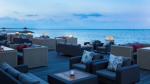 Un salón junto al mar con mobiliario de mimbre y vista al océano.
