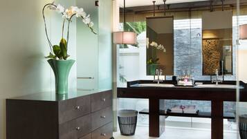 A modern bathroom with a large mirror, dark wooden vanity, and a glass cabinet with orchids.