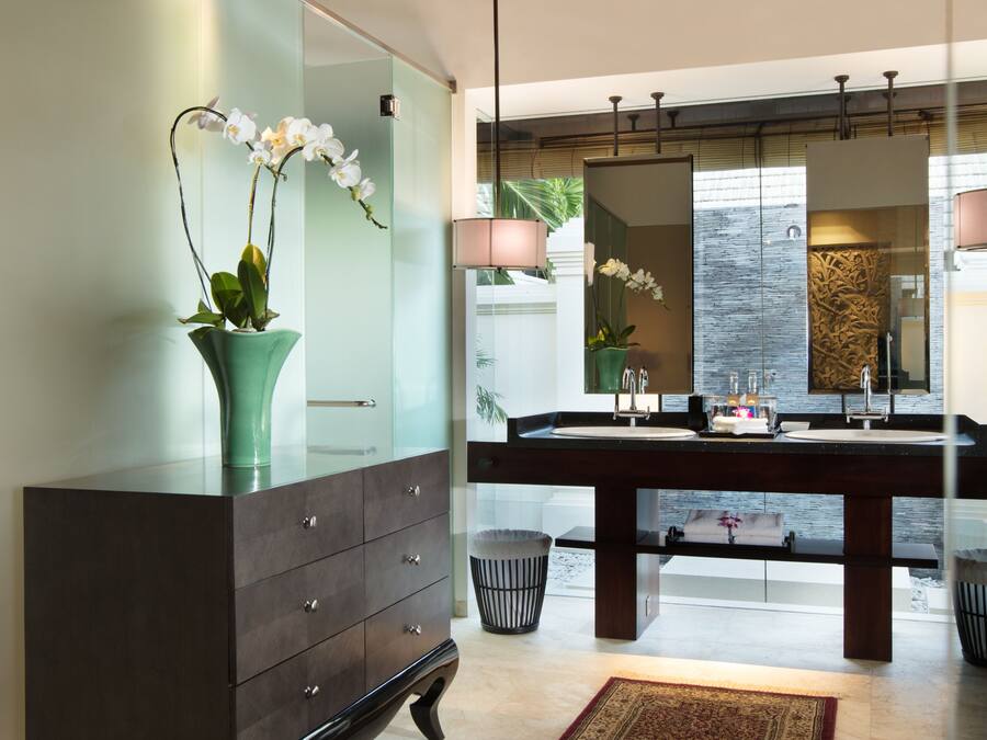 A modern bathroom with a large mirror, dark wooden vanity, and a glass cabinet with orchids.