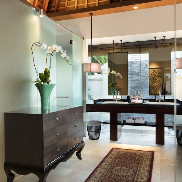 Uma casa de banho moderna com um espelho grande, toucador em madeira escura e um armário de vidro com orquídeas.