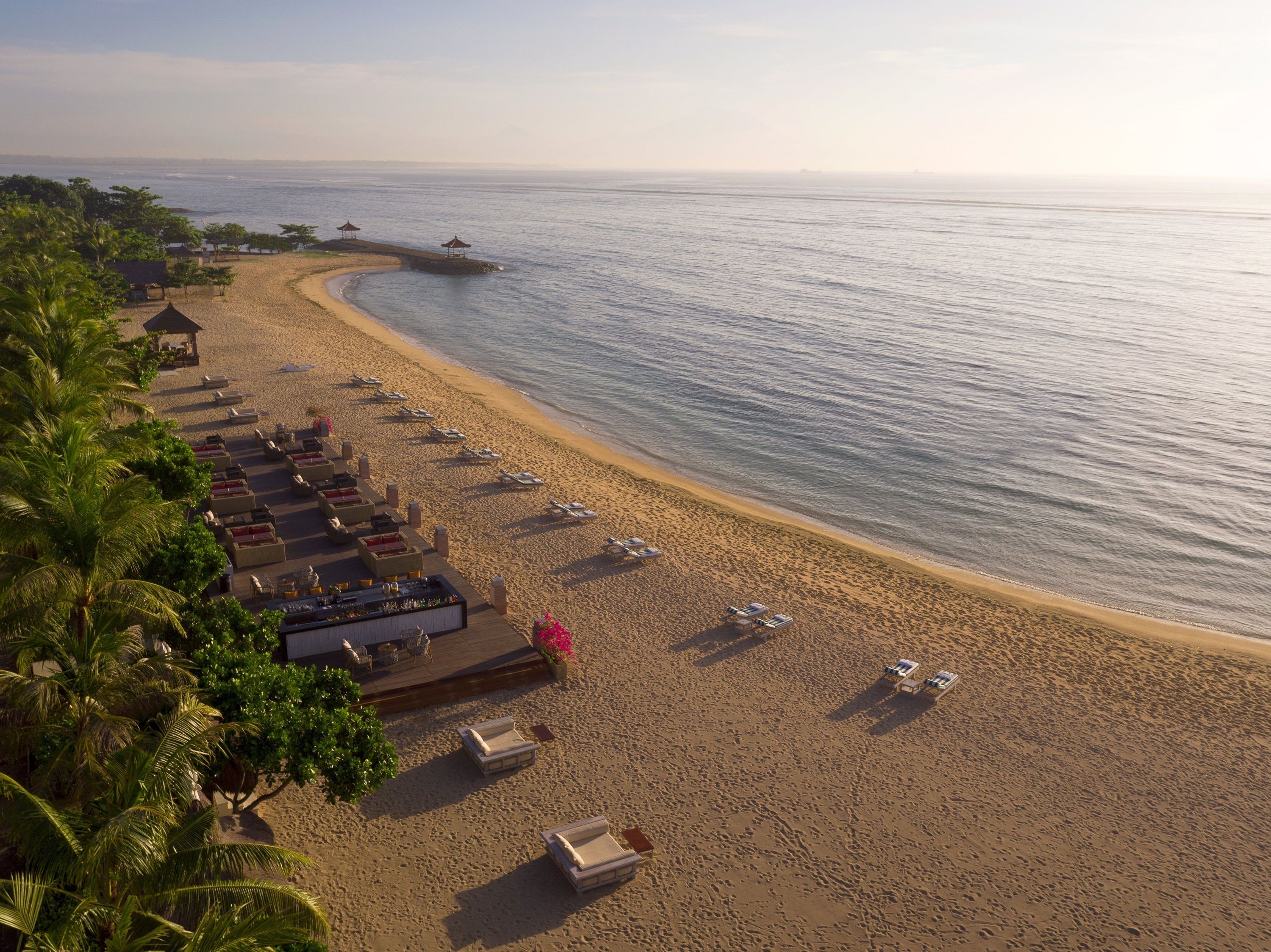 A beach resort with a wooden deck, lounge chairs, and umbrellas.