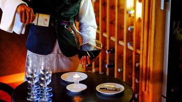 A person pouring wine into glasses on a table with a candle and a plate of cheese.