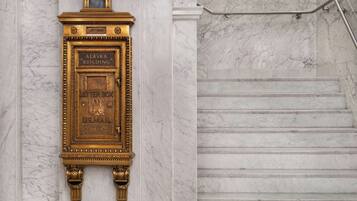 Eine Marmortreppe mit einem goldenen Briefkasten, beschriftet mit 'Alaska Building' und 'U.S. Mail', an der Wand.