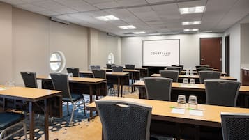 A conference room with multiple tables and chairs, a large screen displaying "COURTYARD BY MARBERRY," and a door to the right.