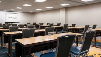 A conference room with multiple tables and chairs, a projection screen, and a carpeted floor.