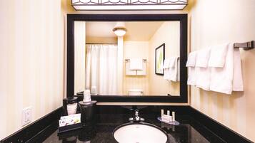 Un baño con un espejo grande, encimera negra, lavabo blanco y un perchero para toallas.