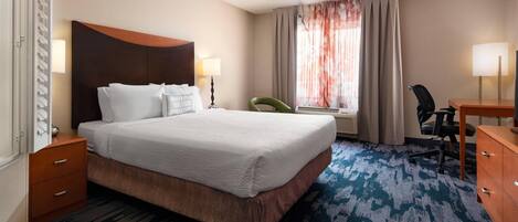 A hotel room with a large bed, a desk, a chair, a lamp, and a window with curtains.