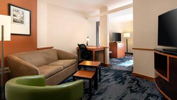 A hotel room with a sofa, a desk, a television, and a lamp.